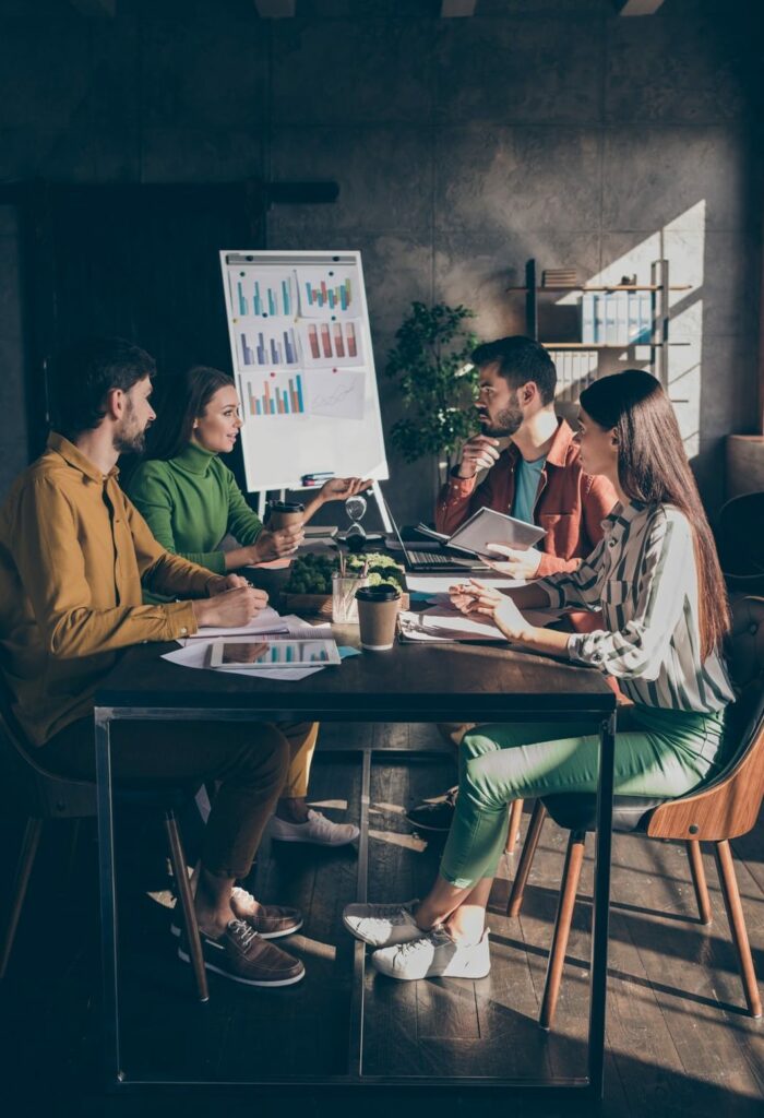 Quatre salarié d'entreprise autour d'une table de réunion devant un paperboard se formant au Management de Projet